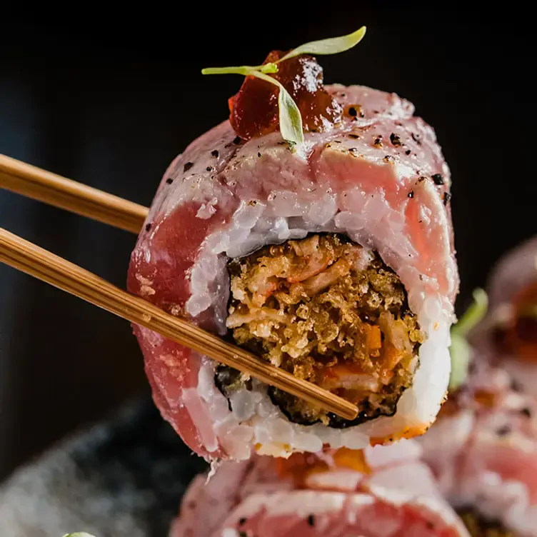 Un rollo de sushi alzado con palillos en Ryoshi, uno de los mejores restaurantes románticos en Monterrey.