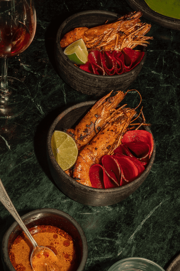 En una mesa de mármol oscuro hay dos cuencos de gambas junto a un cuenco de salsa roja.