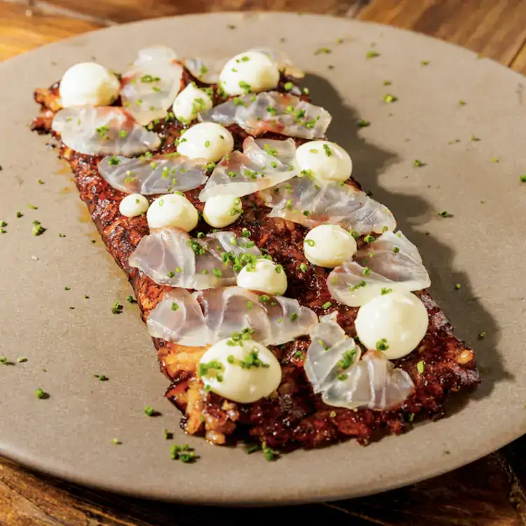 Costra de arroz meloso, rellena de chicharrón prensado con láminas de pescado curado en Aleli Rooftop, ono de los mejores restaurantes al aire libre en la CDMX.