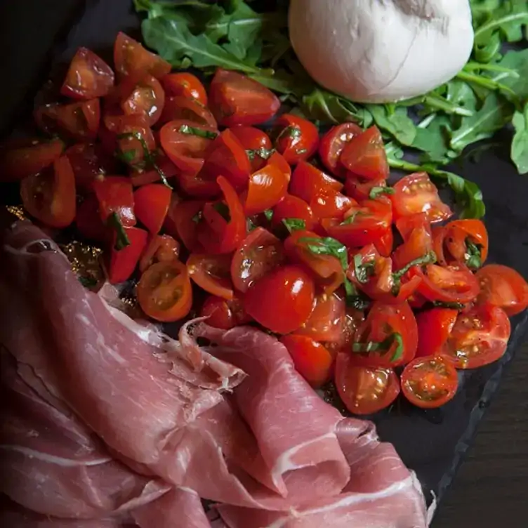 Una tabla italiana de jamón, tomates, ensalada y mozzarella en Lo Spuntino, uno de los mejores restaurantes con terrazas en Monterrey.