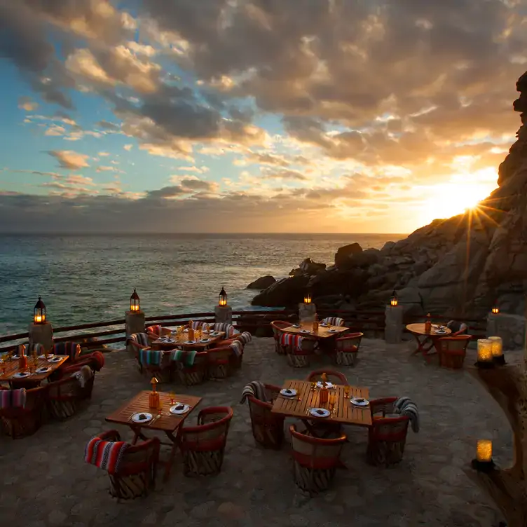 Terraza en la playa de Cabo San Lucas, con mesas y un hermoso atardecer en El Farallon – Waldorf Astoria Los Cabos Pedregal en Los Cabos