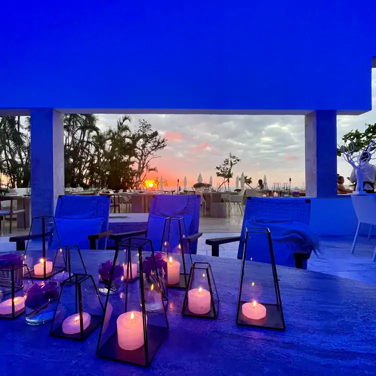 Interiores minimalistas sumergidos en una luz azul, con linternas y el atardecer en el fondo en Origen, uno de los mejores restaurantes en la playa en México