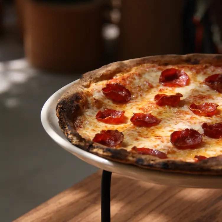 Pizza de pepperoni sobre plato blanco en mesa de madera en el restaurante BAM BAM PIZZA, uno de los mejores restaurantes baratos de CDMX.