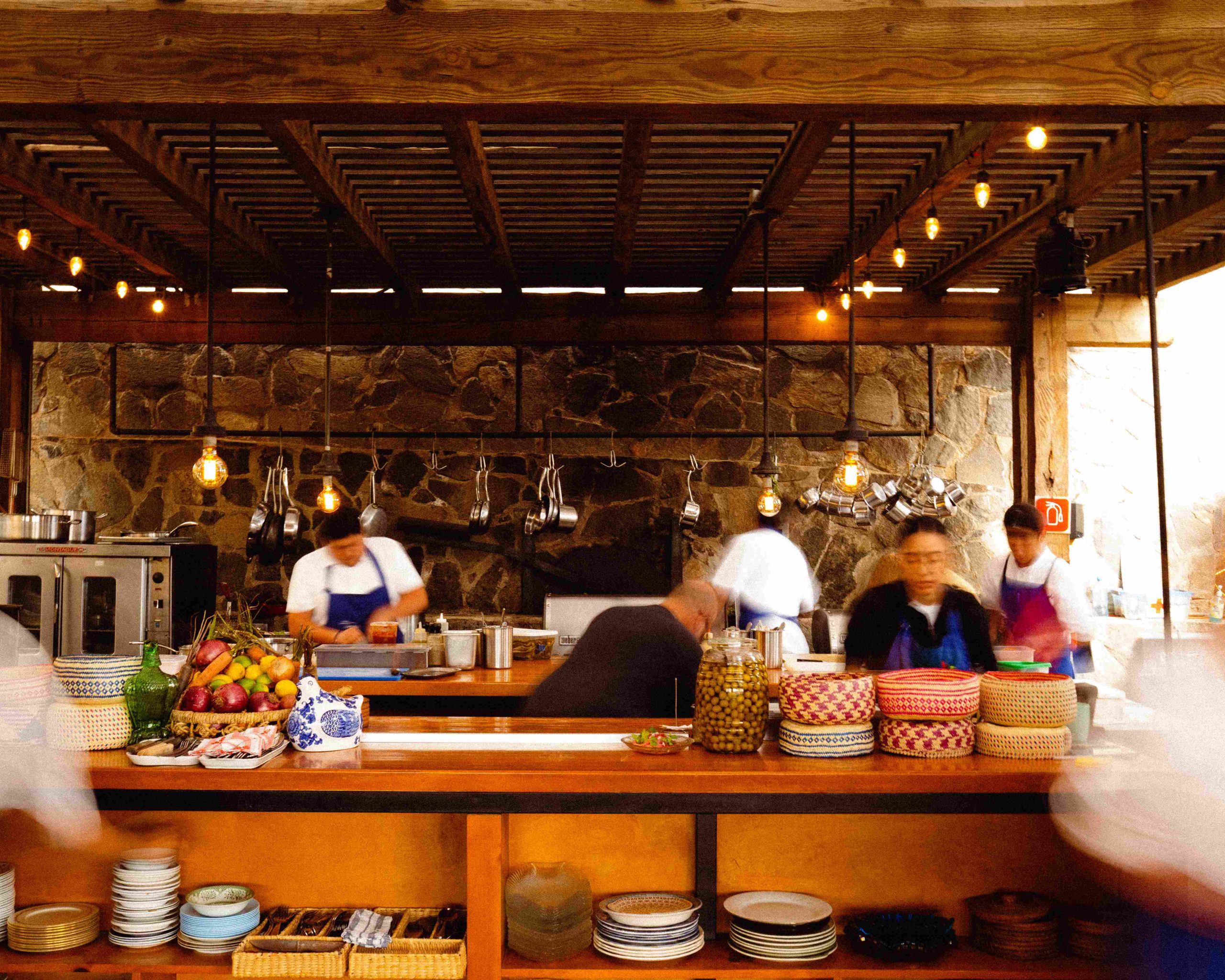 Cocineros trabajando en una cocina abierta con pared de piedra en Villa Torél en el Valle de Guadalupe