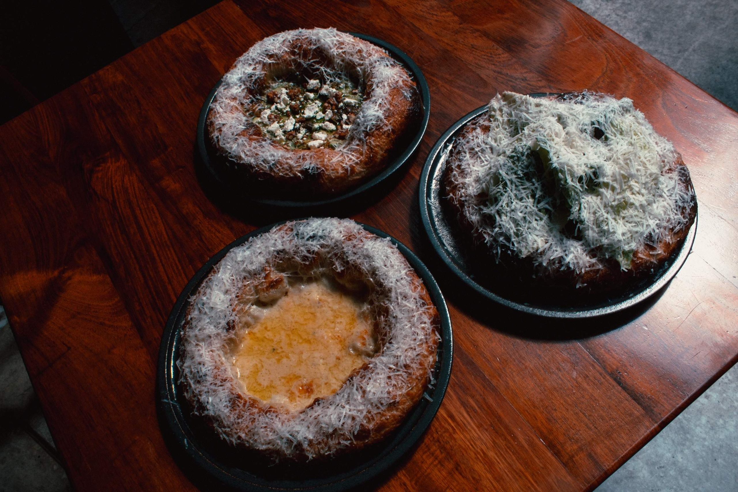 Tres pizzas de bordes gruesos sobre una mesa de madera en el restaurante ANONIMO COLECTIVO