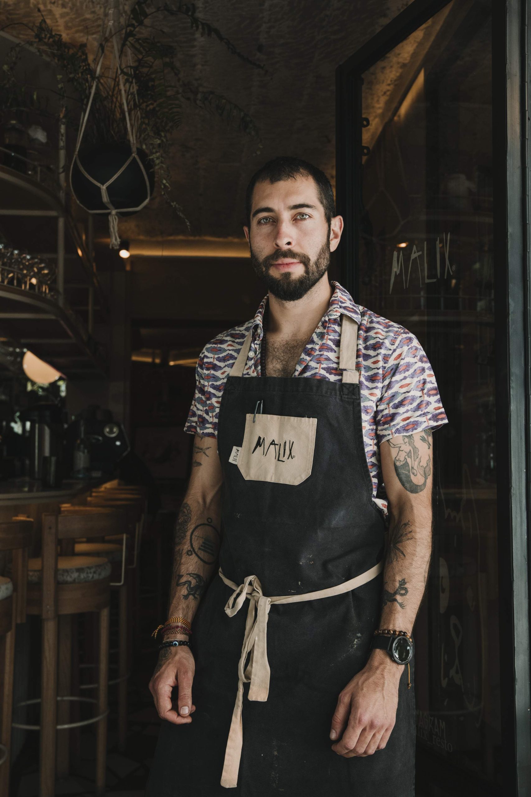 El chef de Malix, Alonso Madrigal vestido con delantal negro y tatuajes en sus brazos, posando para la foto para el Dia del chef