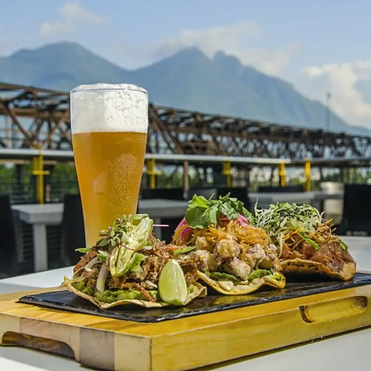 Una tabla con 3 tostadas, una cerveza fría y al fondo el cerro de la silla en el restaurante El Lingote