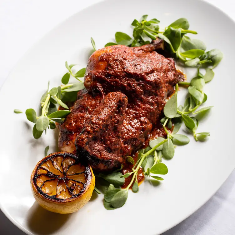 Un plato de carne adobada, con hierbas y una rodaja de limón tatemado, todo finamente presentado