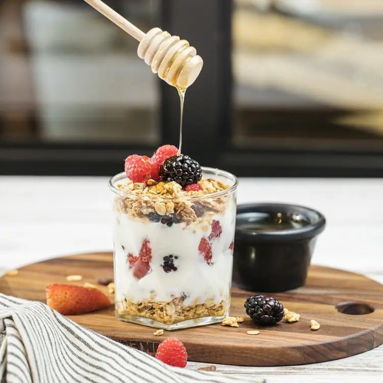 Un frasco de yogurt, granola y frutos rojos sobre el que cae un chorro de miel de abeja. Éste es uno de los platillos de Los Canarios, uno de los mejores restaurantes para desayunar en CDMX.