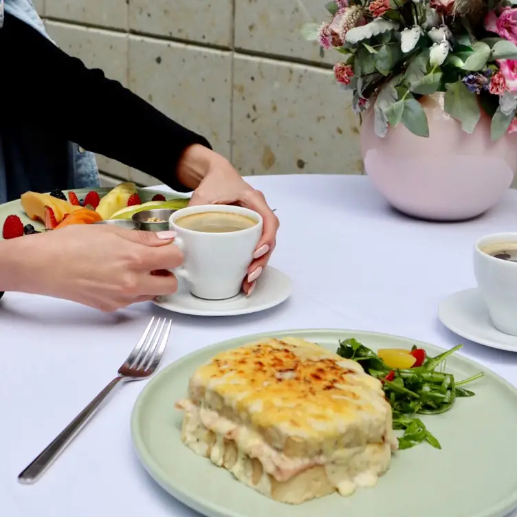 Una mesa de Jardín Alba, uno de los mejores restaurantes para desayunar delicioso en CDMX, en la que se muestra un café, un plato de frutas y un sándwich con queso gratinado