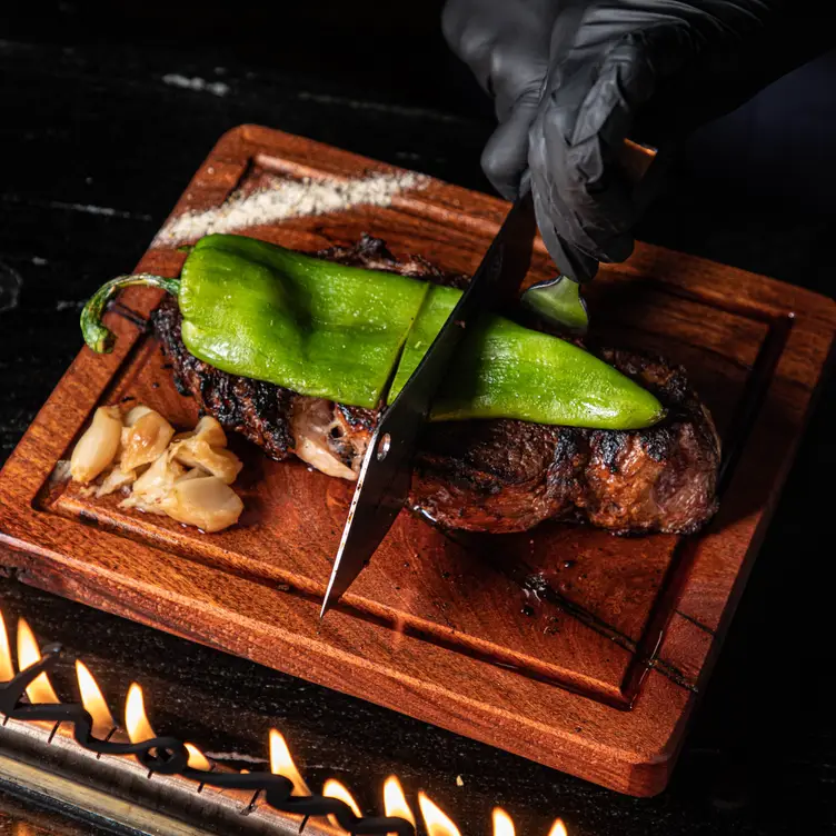 Unas manos con guantes cortando un corte de carne sobre una table en Mochomos-Monterrey, una de las mejores opciones sonorenses para comer