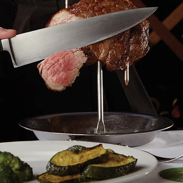 Un mesero de Fogo de Chao rebanando un trozo de carne de una espada directo hacia un plato