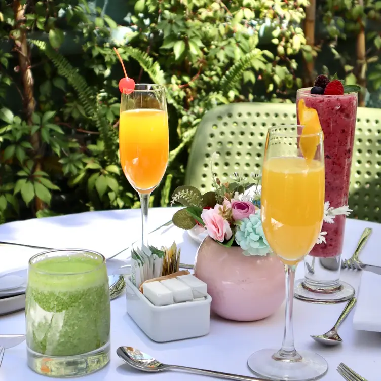 Mesa exterior de Jardín Alba, uno de los mejores restaurantes para desayunar en CDMX, en donde se puede ver un jugo verde, dos copas de mimosas y un smoothie de frutas