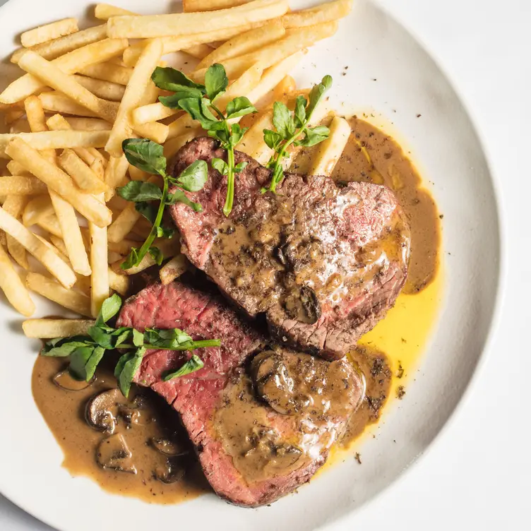 Un plato de carne con salsa de champiñones, hierbas y papas fritas en Colmillo, uno de los mejores restaurantes de carnes en CDMX.