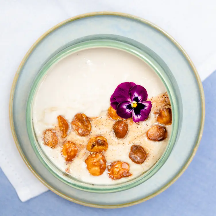 Yogurt vegano de coco con macadamia caramelizada.webp: Un plato de yogurt vegano con nueces de macadamia y una flor morada en Casa Ó – Lomas, uno de los mejores restaurantes para desayunar en CDMX