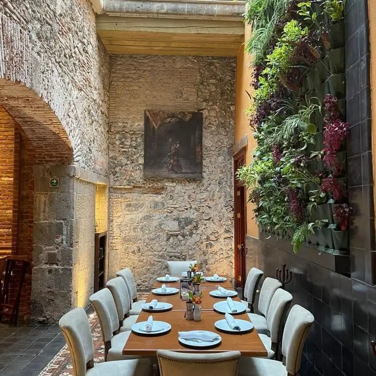 Interior del restaurante Saks, uno de los mejores en CDMX para desayunar, donde se aprecia una mesa larga, una pintura clásica y un jardín vertical cubierto de piedras.