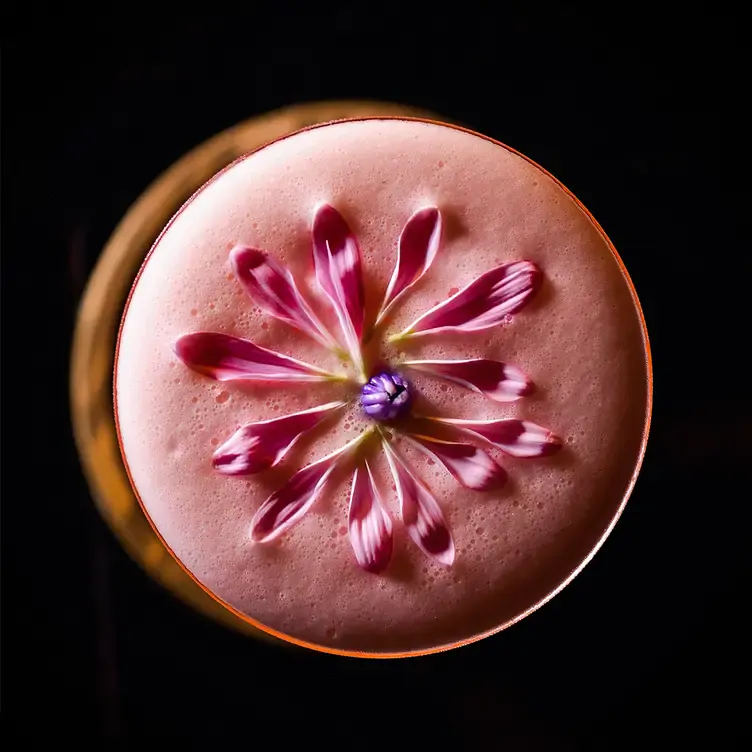 Un coctel visto desde arriba con espuma rosa y adornada con pétalos de flor en Flamel, uno de los mejores restaurantes románticos en Mérida.