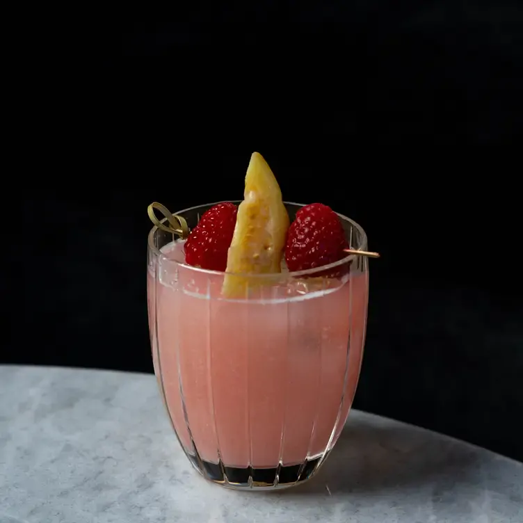 Un vaso con agua de frutas con un pedazo de guayaba y dos frambuesas.