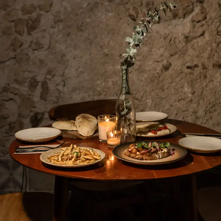 Una mesa a media luz servida con distintos platillos, una vela y un florero en Vana, uno de los mejores restaurantes románticos en Mérida.