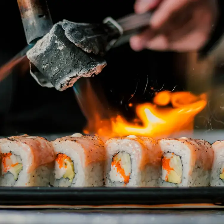 Un rollo maki de varios ingredientes siendo flameado en la mesa, casi listo para ser comido.