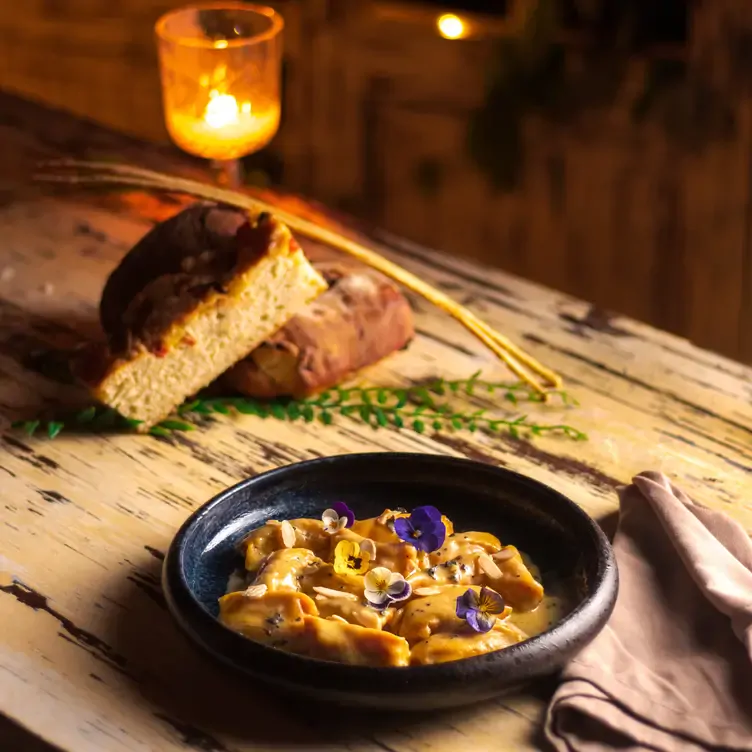 Un plato de pasta, pan y una vela sobre una mesa de madera en Parole Polanco, uno de los mejores restaurantes en CDMX.