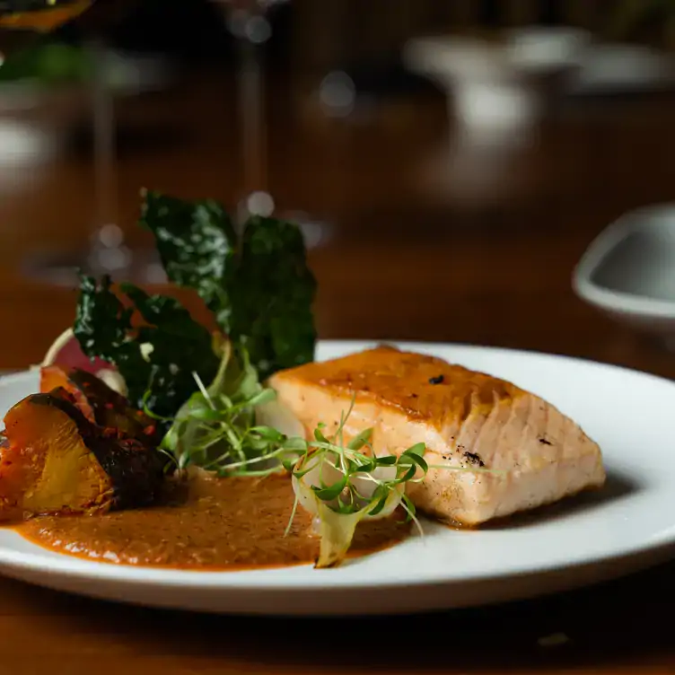 Un trozo de pescado con acompañamiento de salsa y diversos vegetales en Picheta.