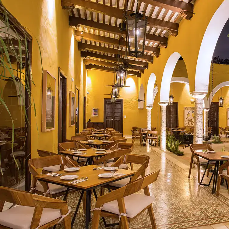 Vista del patio interior del Museo de la gastronomía yucateca, con portales coloniales de colores amarillo pastel con blanco y mobiliario de madera.