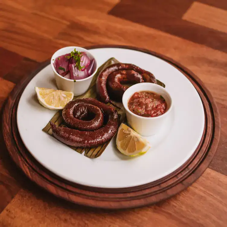 Un plato blanco sobre una mesa de madera con chistorra en hoja de plátano, naranjas y salsas en el Museo de la gastronomía yucateca, una de las mejores opciones para comer en Mérida.