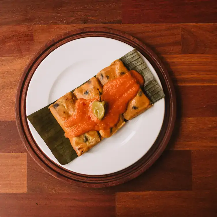 Un plato con tres tamales rojos en hoja de plátano, con salsa y chile habanero en el Museo de la gastronomía yucateca.