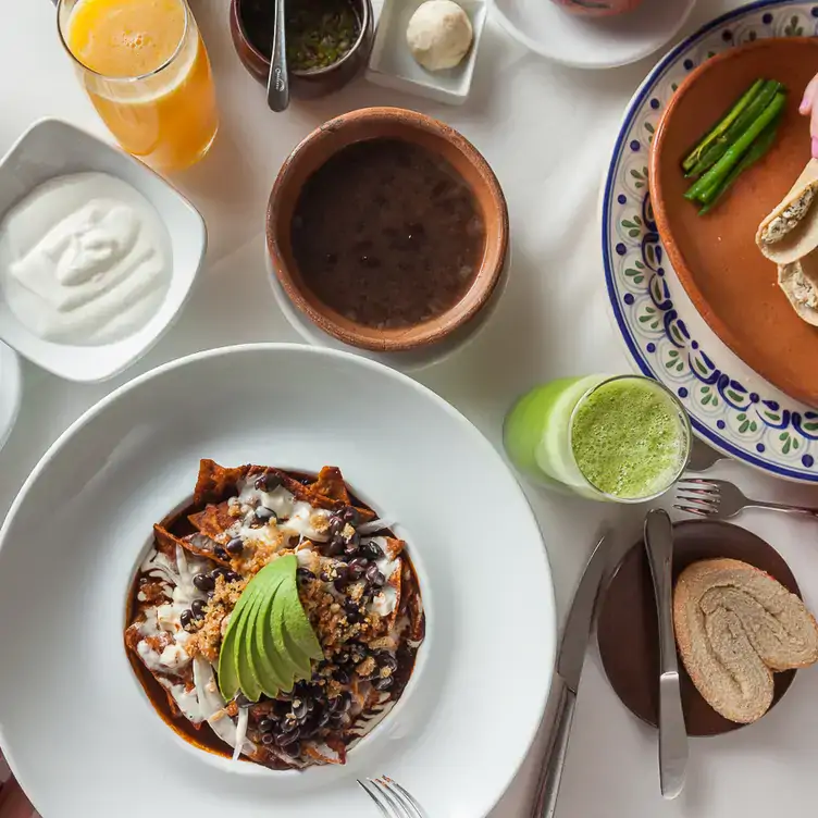 Unos chilaquiles en chile pasilla con frijoles de olla a un costado en El Mural de los Poblanos, uno de los mejores restaurantes para desayunar en Puebla.