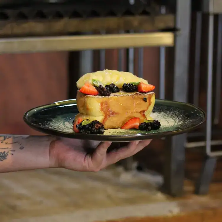 Una mano alzando un plato de un postre con frutas en Jumiles Experiencia Mexicana, uno de los mejores restaurantes para desayunar en Mérida.