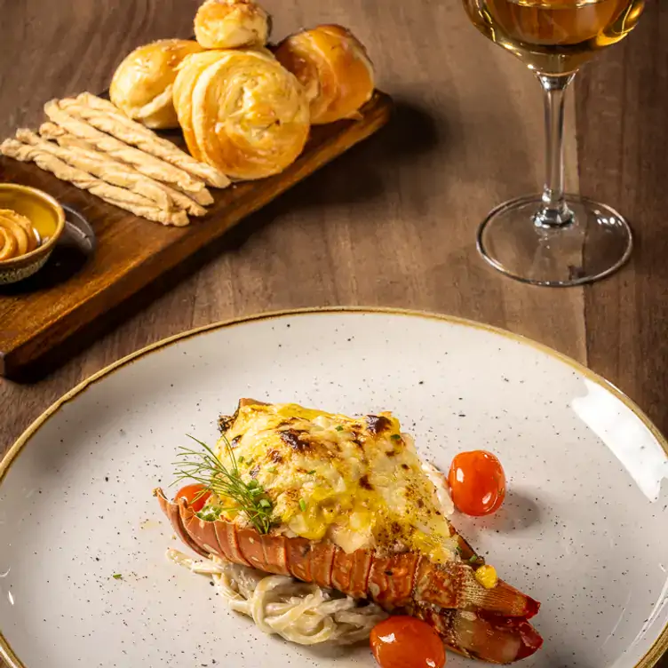 Platillo de langosta, acompañado de una copa de vino blanco y una selección de pan en Crab House Cancún.