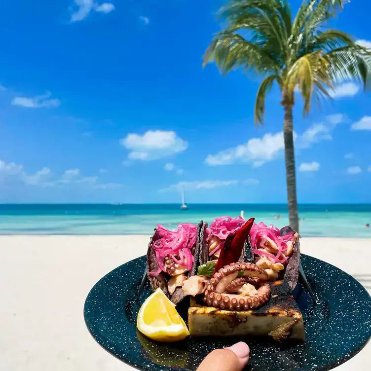 Tres tacos de pulpo acompañados de limón y cebolla morada, con la orilla del mar como paisaje en Caribeño Cancún, uno de los mejores restaurantes para desayunar en Cancún.