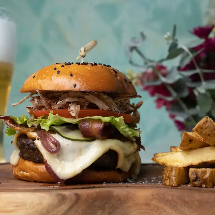 Una hamburguesa con un medallón de carne, queso, tocino, lechuga y jitomate, acompañada de papas fritas en Leynia, uno de los mejores restaurantes para el brunch en Cancún.