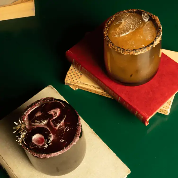 Dos vasos de coctel escarchados en Café Pia, con dos libros sobre una mesa verde.