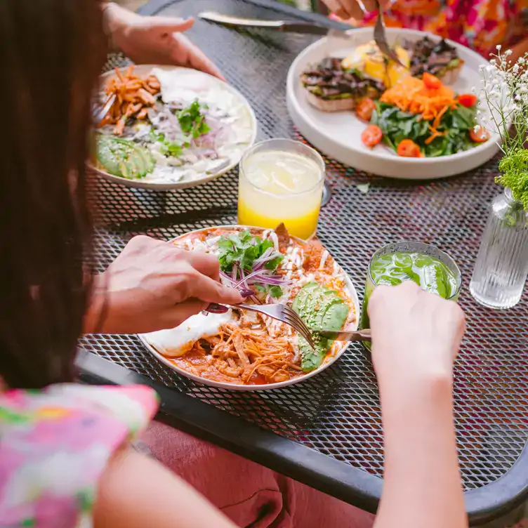 Tres personas en una mesa comiendo tres distintos platillos con bebidas y un florero.