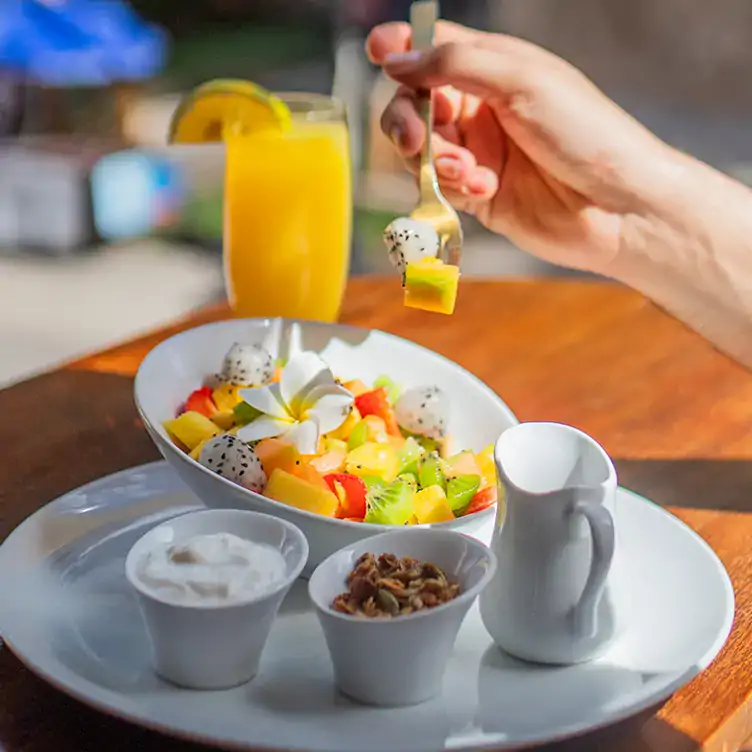 La mano de una persona con un tenedor comiendo fruta con yogurt y un jugo en Le Makech, uno de los mejores lugares de desayunos en el centro de Mérida.