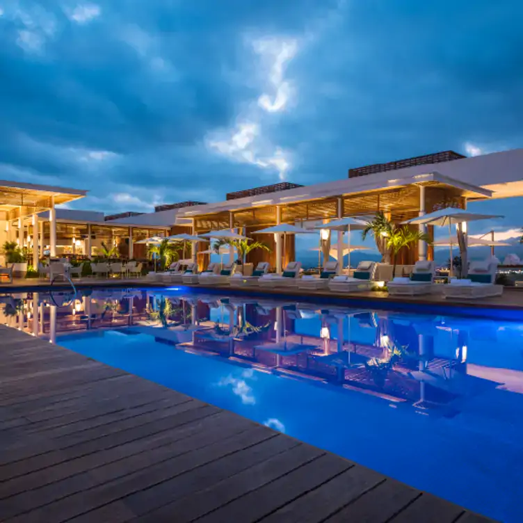 Vista después del atardecer de la piscina del Quinto at Vidanta Nuevo Vallarta y al fondo las mesas del restaurante.