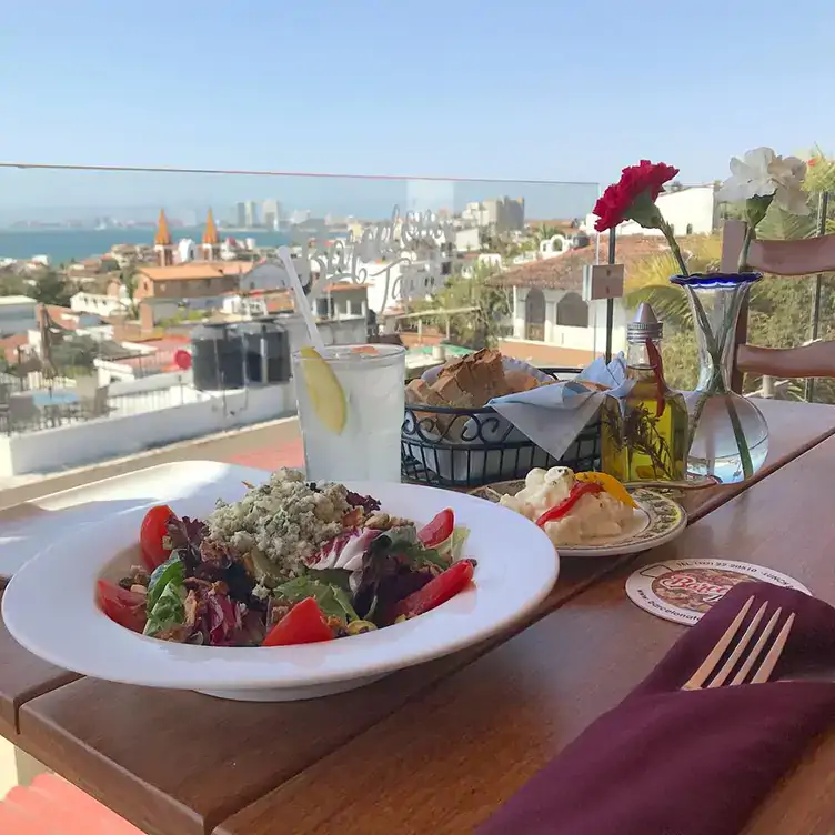 Platillos y bebidas servidos en lo alto, con una vista panorámica de Puerto Vallarta y el mar al fondo.