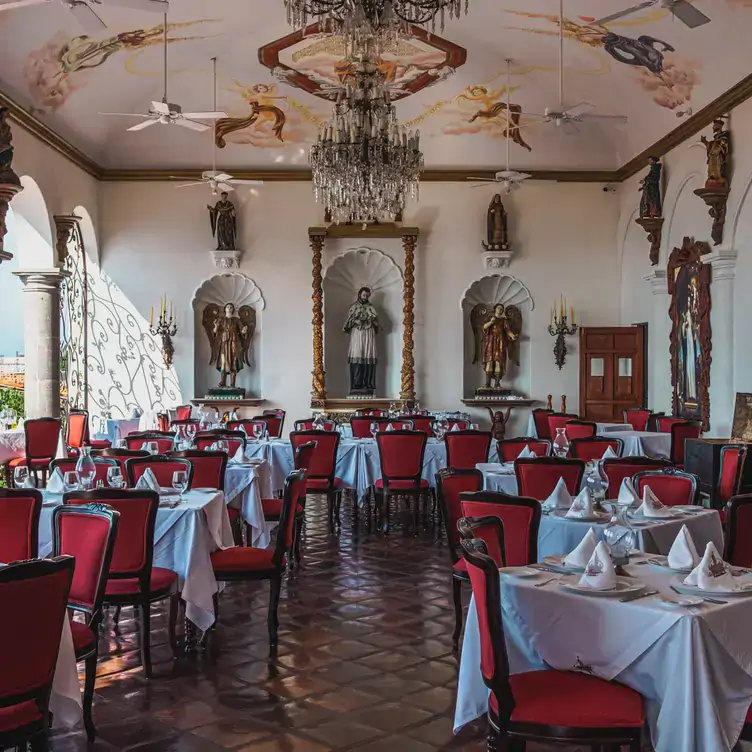 Sillas de madera tapizadas en rojo, mesas blancas y ornamentación sacra en La Cappella, de los mejores restaurantes en Puerto Vallarta.