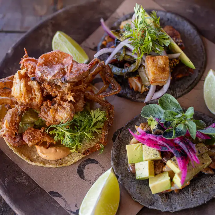 Tres tacos abiertos con varios rellenos, incluyendo cerdo y aguacate en Punta Corcho, un restaurante que fue galardonado con un premio Bib Gourmand de la Guía MICHELIN.