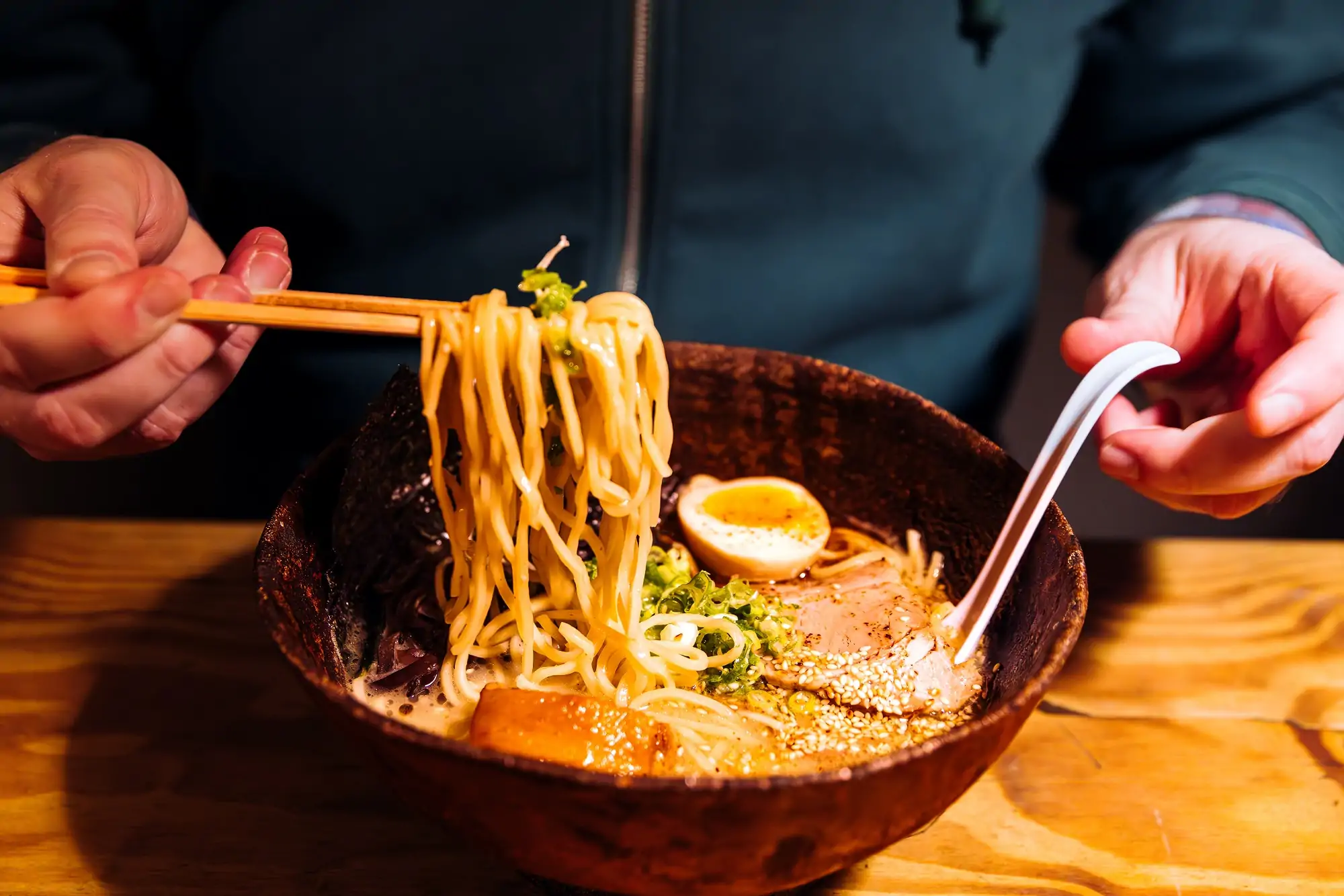 Un tazón de ramen tradicional, servido con fideos, láminas de cerdo ahumado, huevo cocido y cebollín, ¡listo para degustar con los clásicos palillos!