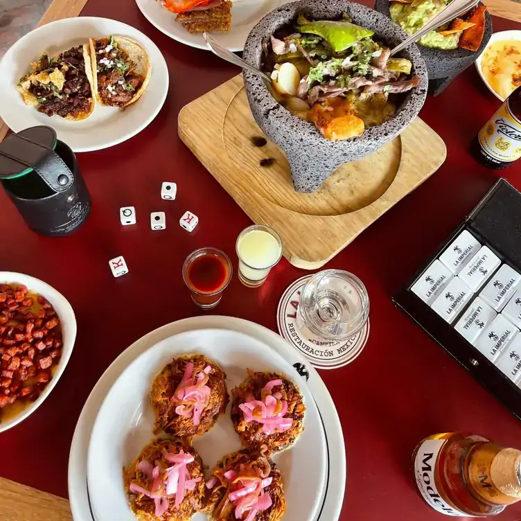 Vista desde arriba de una mesa servida con una variedad de platillos para compartir, bebidas y juegos de mesa en La Imperial, uno de los mejores restaurantes para grupos en la CDMX.