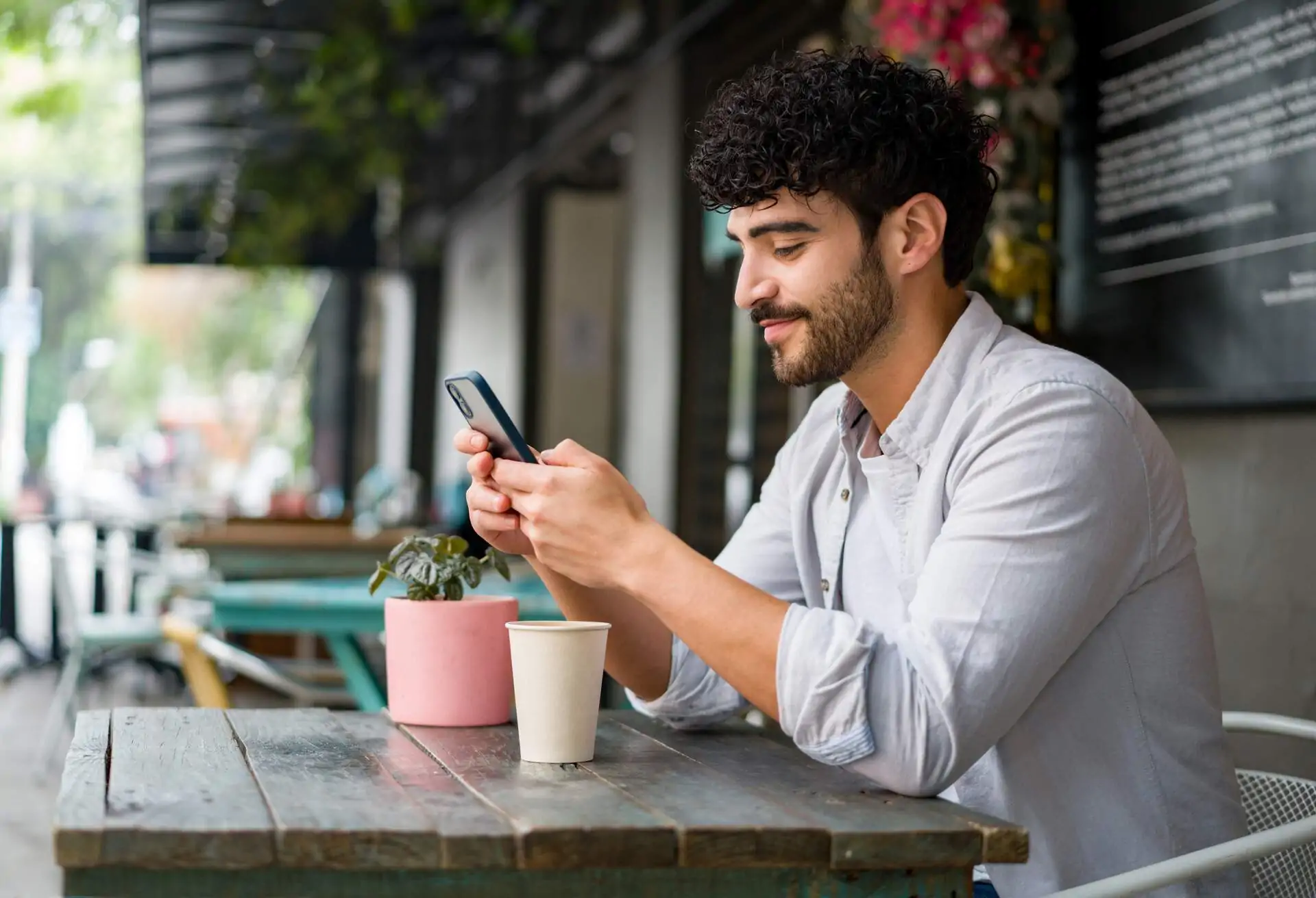 Hombre sentado en el libre aire en un restaurante con su movil.